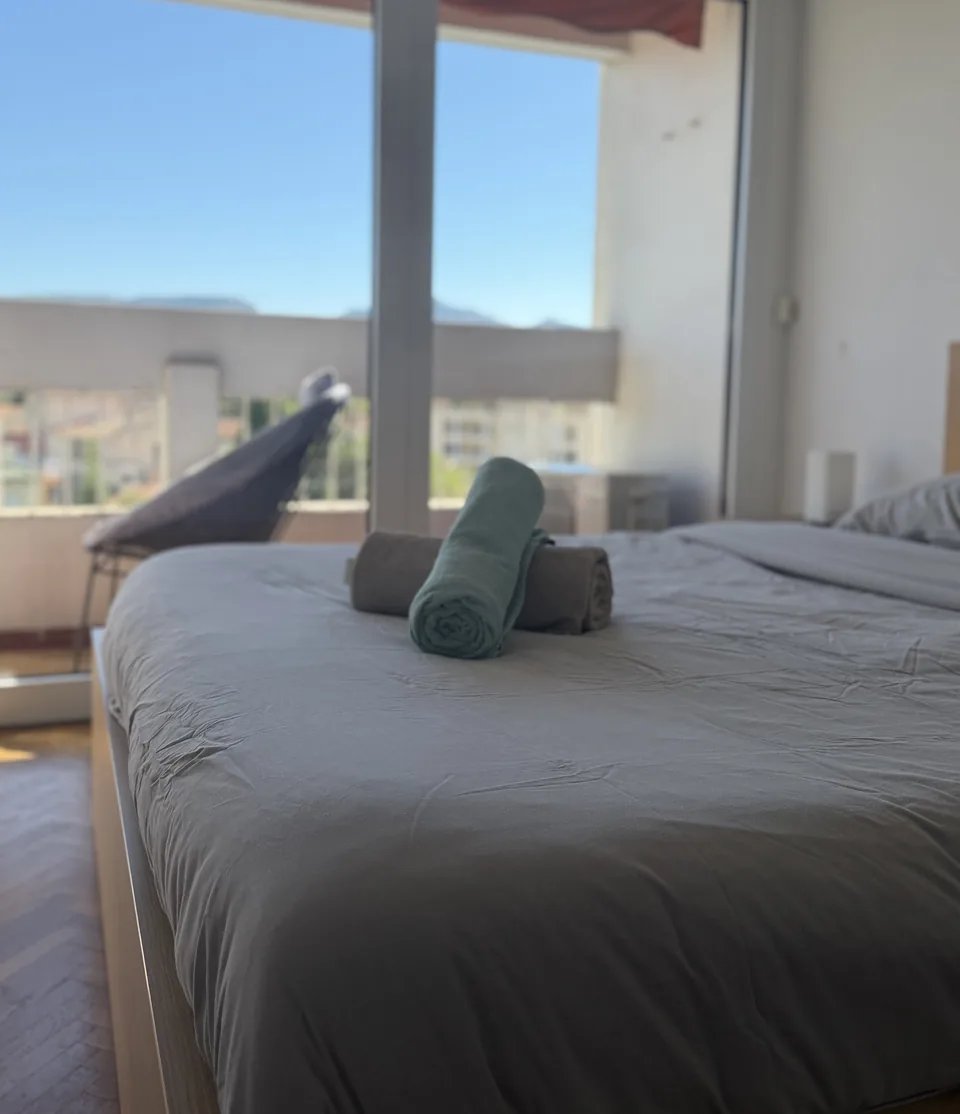 Chambre ouverte sur un balcon et le ciel bleu, serviettes roulées posées sur le lit