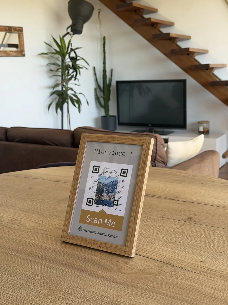 Cadre « Bienvenue » avec code QR menant au livret d'accueil numérique, posé sur une table en bois
