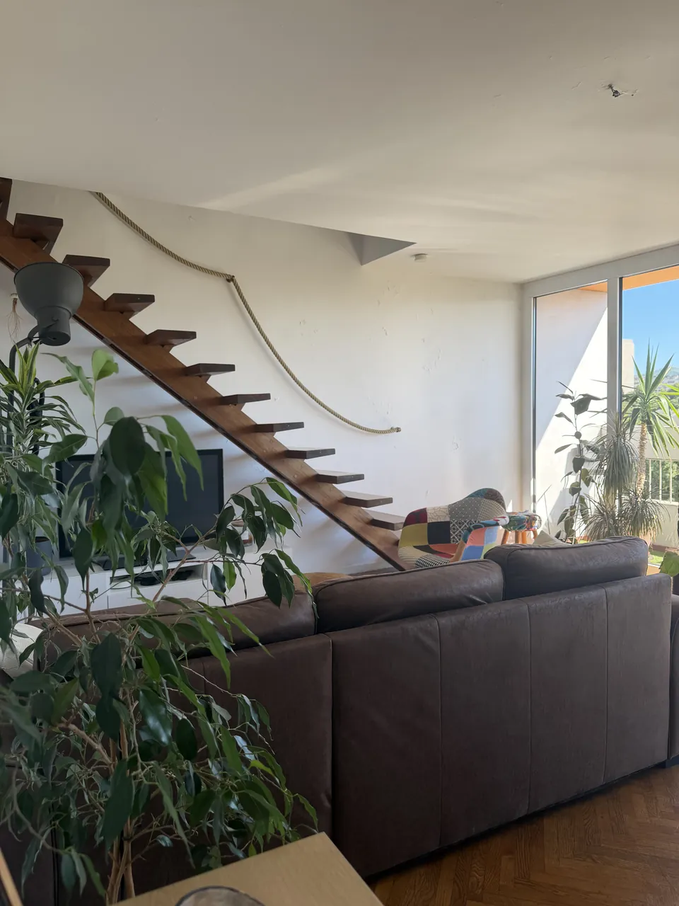Séjour lumineux d'un appartement géré par Ben&Co, escalier suspendu en bois, canapé et grande baie vitrée ouverte sur le ciel de Marseille